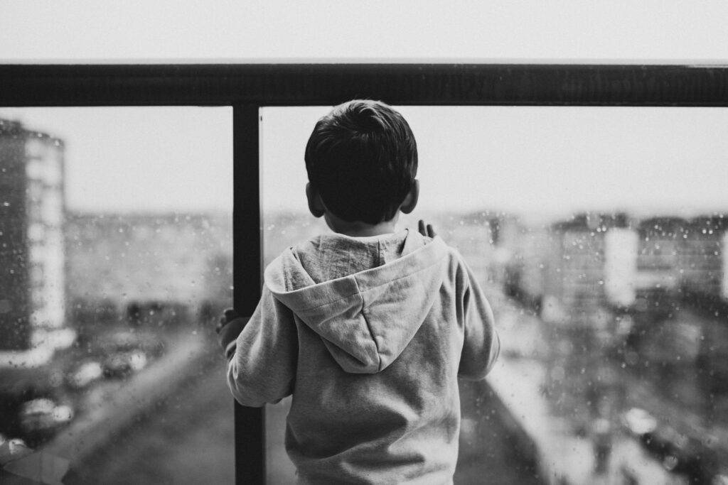 A little boy looking out a window down on the city on a rainy day.