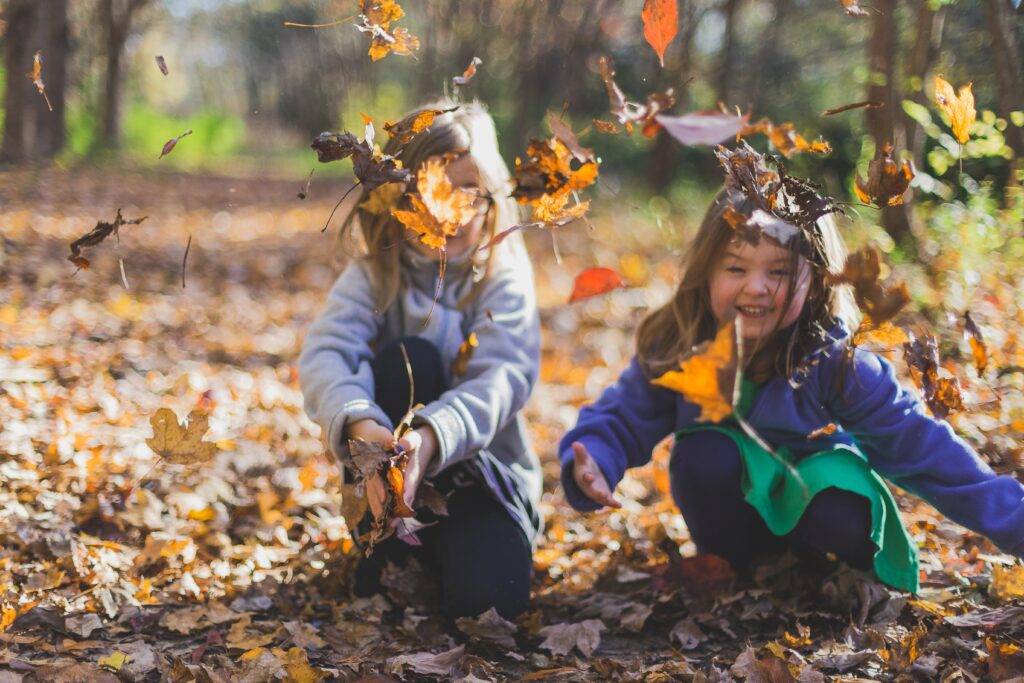 Innocent children playing in the leaves on a crisp autumn day.