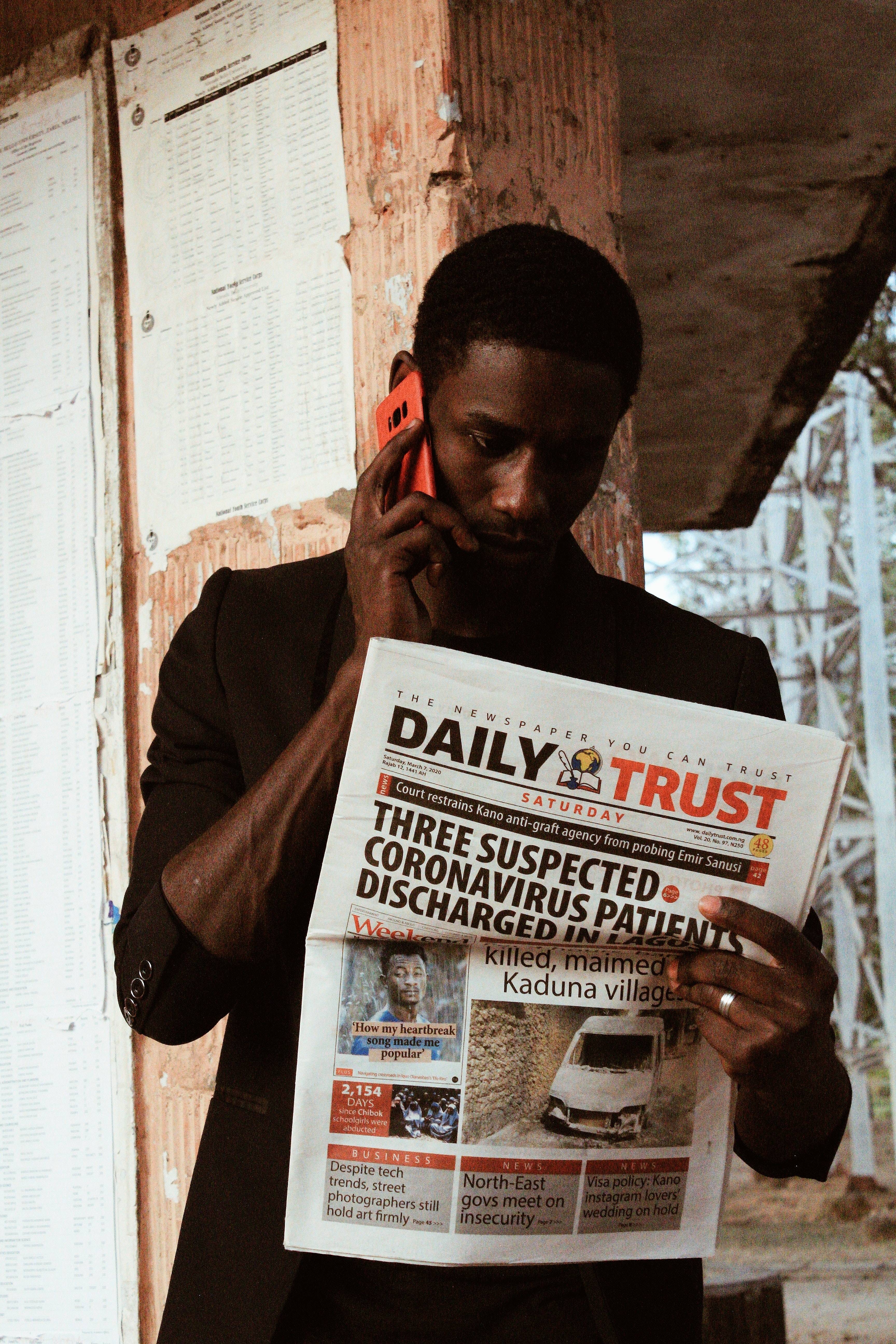 Man reading a tragic newspaper story headlines while taking on the phone.