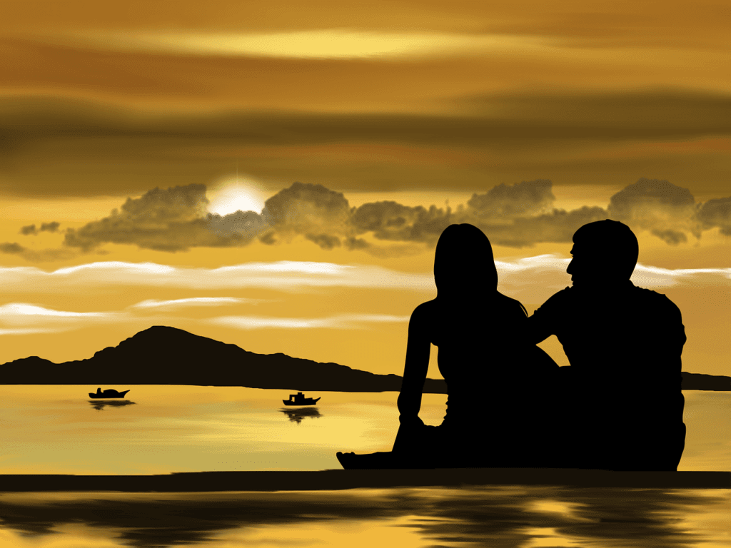 Couple gazing out on the beach at boats during sunset on an island.